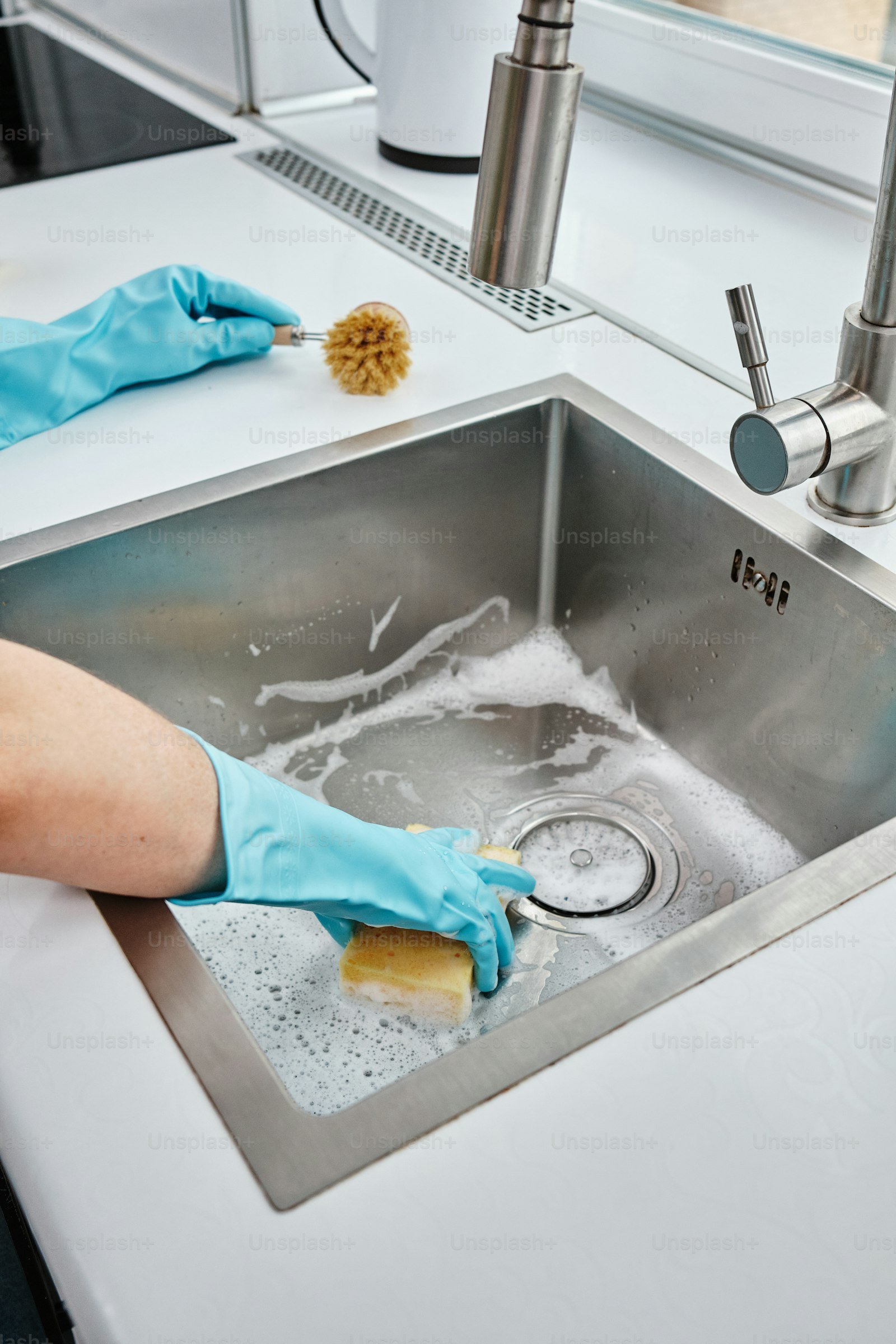 Blue gloves cleaning stainless kitchen sink